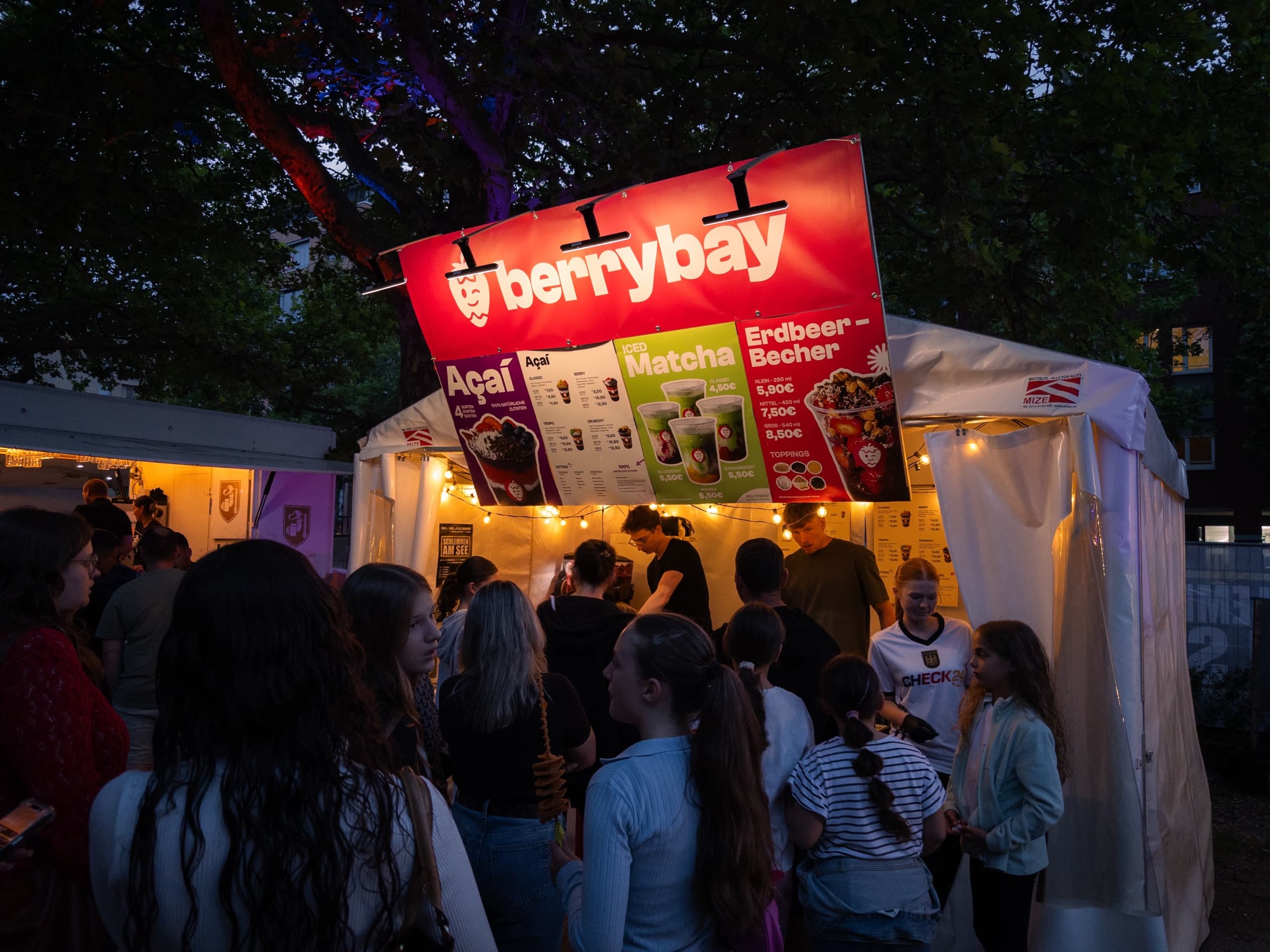 Der beleuchtete Berrybay-Stand am Abend mit wartenden Gästen